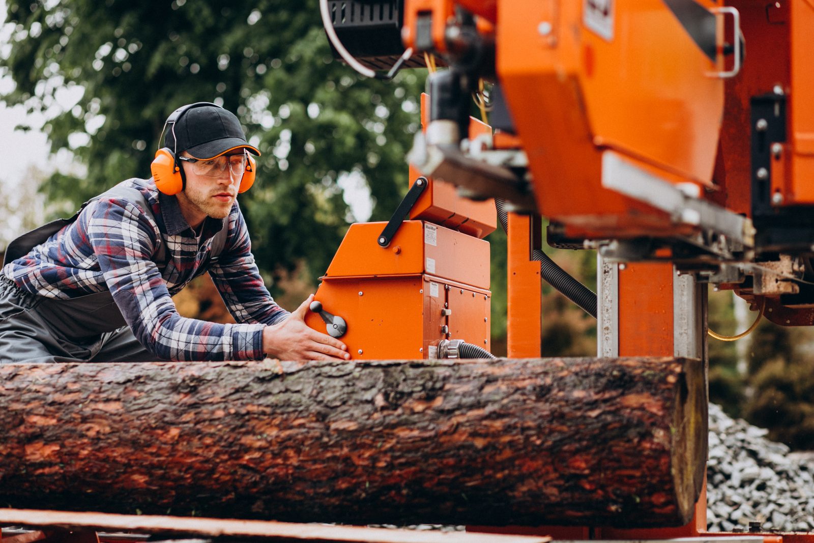 Worker wearing ear protection and safety glasses operating a portable sawmill beside a log